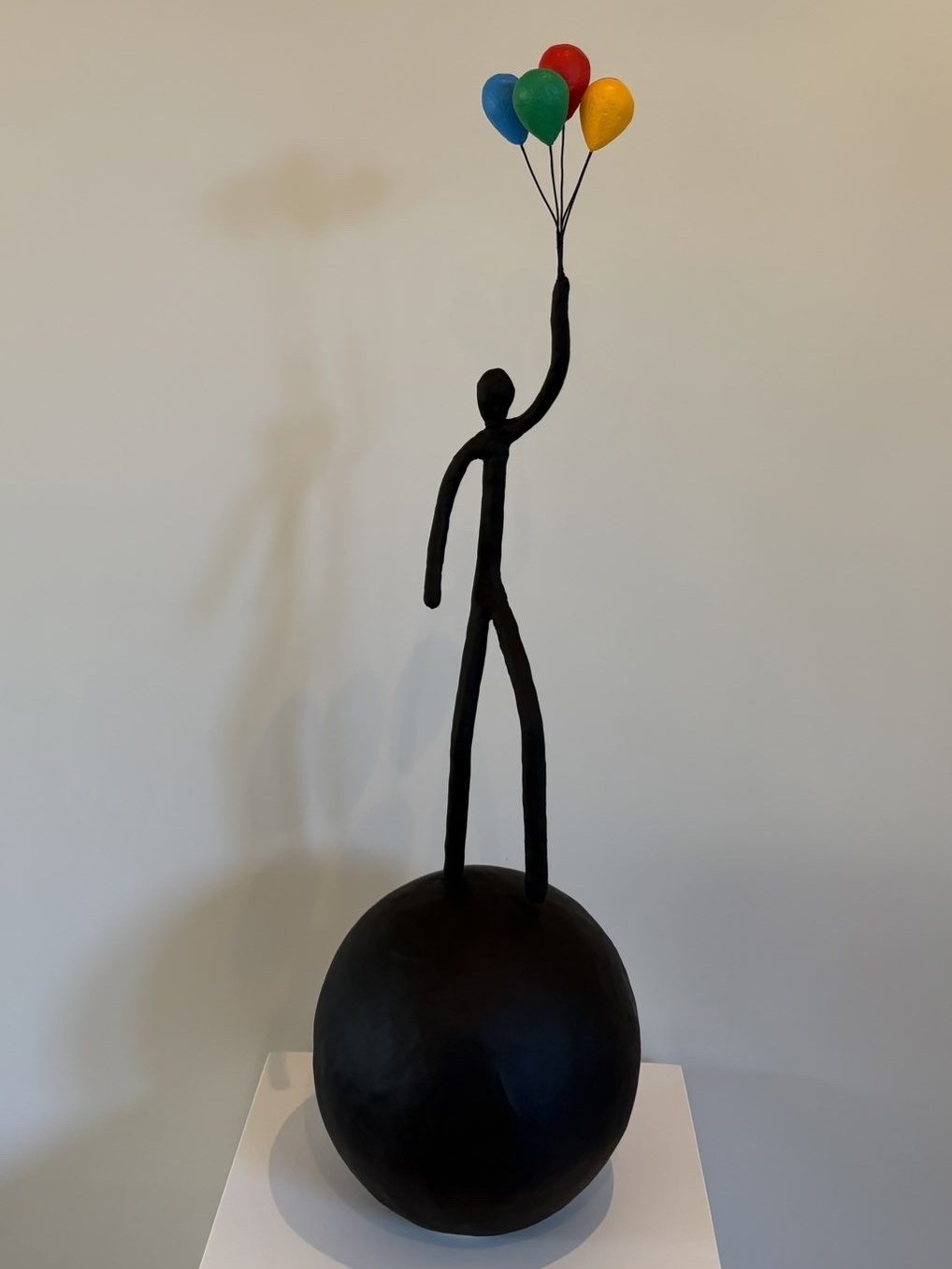 Personnage debout sur une sphère noire tenant quatre ballons colorés